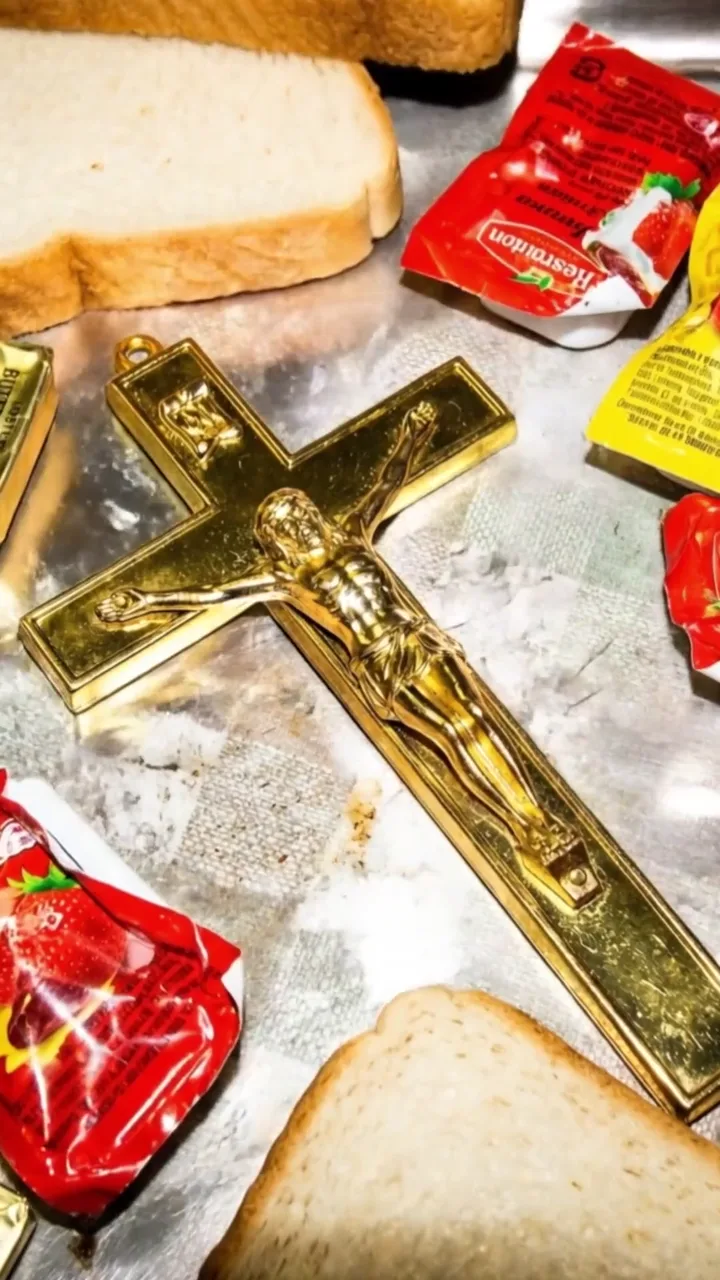 Un crucifijo dorado sobre una bandeja de metal con pan de molde y kétchup.